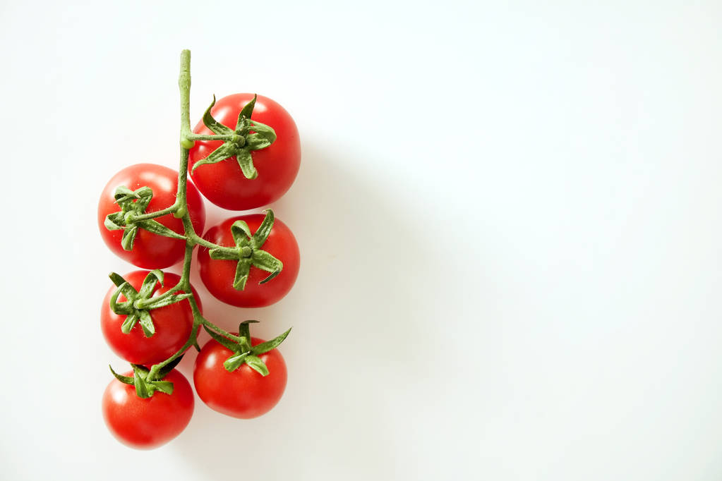 Composición plana minimalista de tomates cherry rojos brillantes que reflejan la luz, colocando sobre la mesa blanca sólida
. - Foto, Imagen