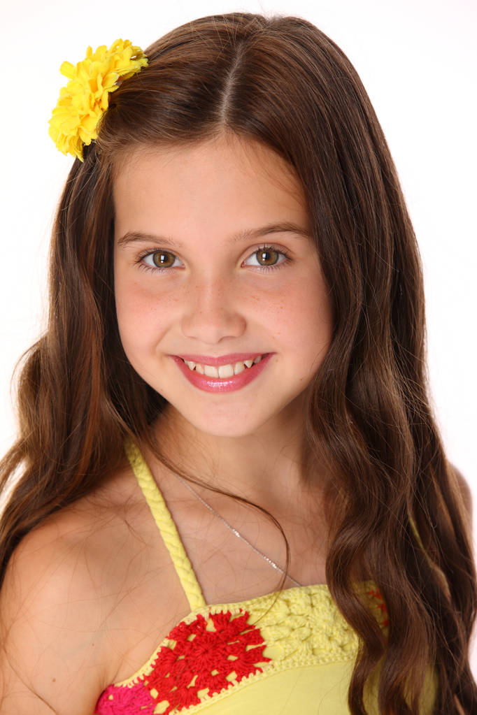 Bir güzel şirin mutlu genç genç kız sarı bir üst ve çiçek-pin yakın çekim portresi. Şık uzun saçlı sevimli esmer çocuk şakacı bakar ve gülümser. - Fotoğraf, Görsel