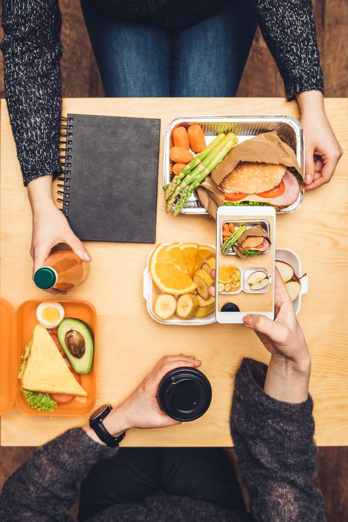 oříznutý obraz žena sedí u stolu a pořizování Foto oběda s smartphone - Fotografie, Obrázek