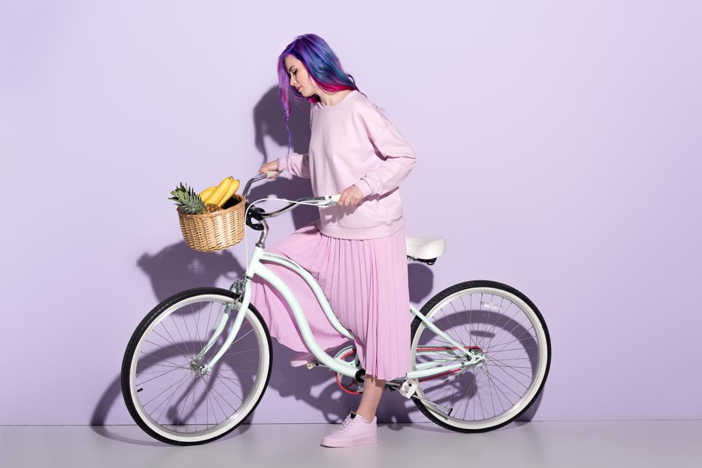 viehättävä nuori nainen vaaleanpunaisissa vaatteissa polkupyörällä ananaksella ja banaaneilla korissa
 - Valokuva, kuva