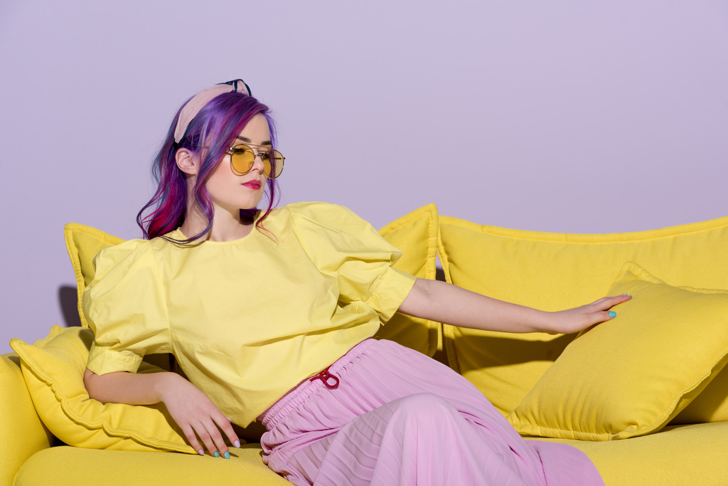 beautiful young woman in yellow eyeglasses sitting on yellow couch - Photo, Image