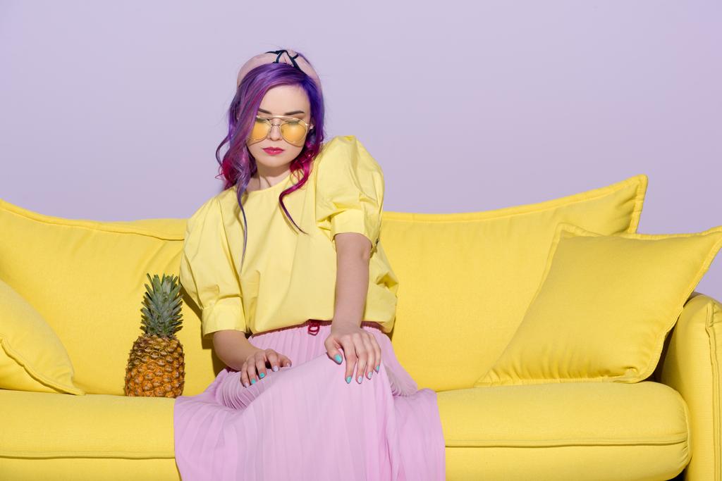divatos fiatal nő ül sárga kanapén, ananásszal - Fotó, kép