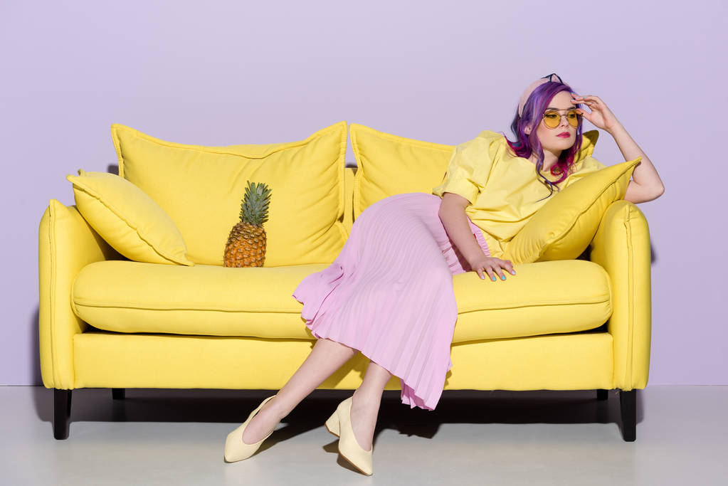 elegante mujer pensativa sentada en un sofá amarillo con piña
 - Foto, Imagen
