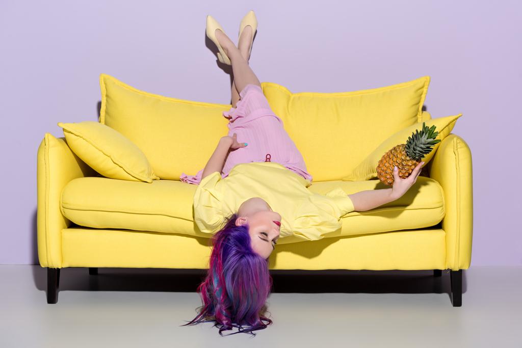 όμορφη νεαρή γυναίκα ξαπλωμένη ανάποδα στον κίτρινο καναπέ με ανανά - Φωτογραφία, εικόνα