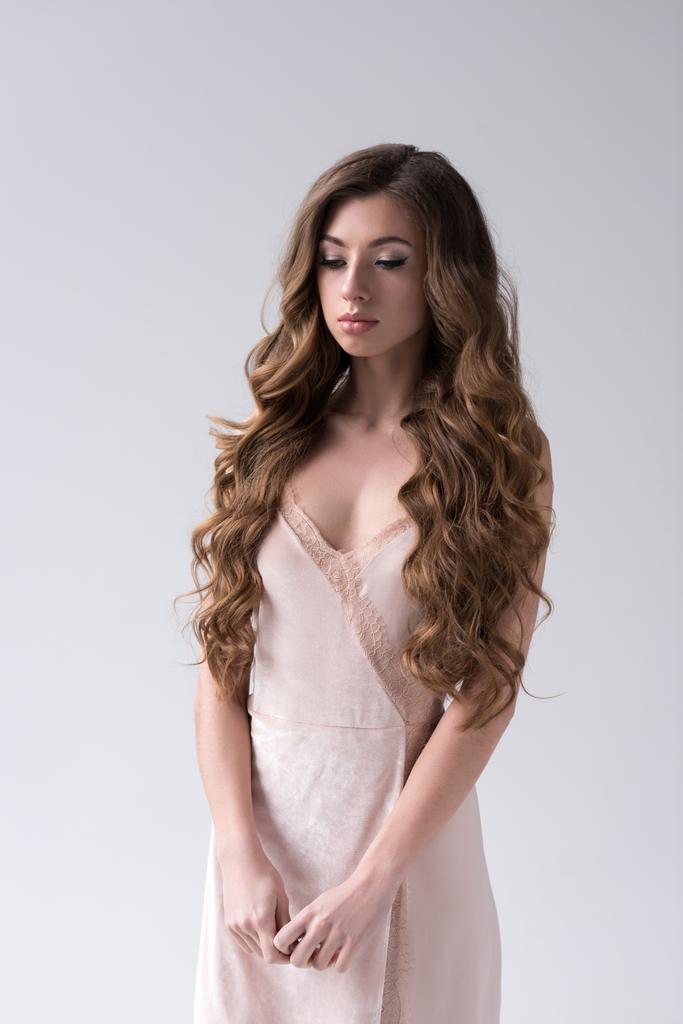 modelo rizado atractivo con el pelo largo posando en vestido rosa, aislado en gris
 - Foto, imagen