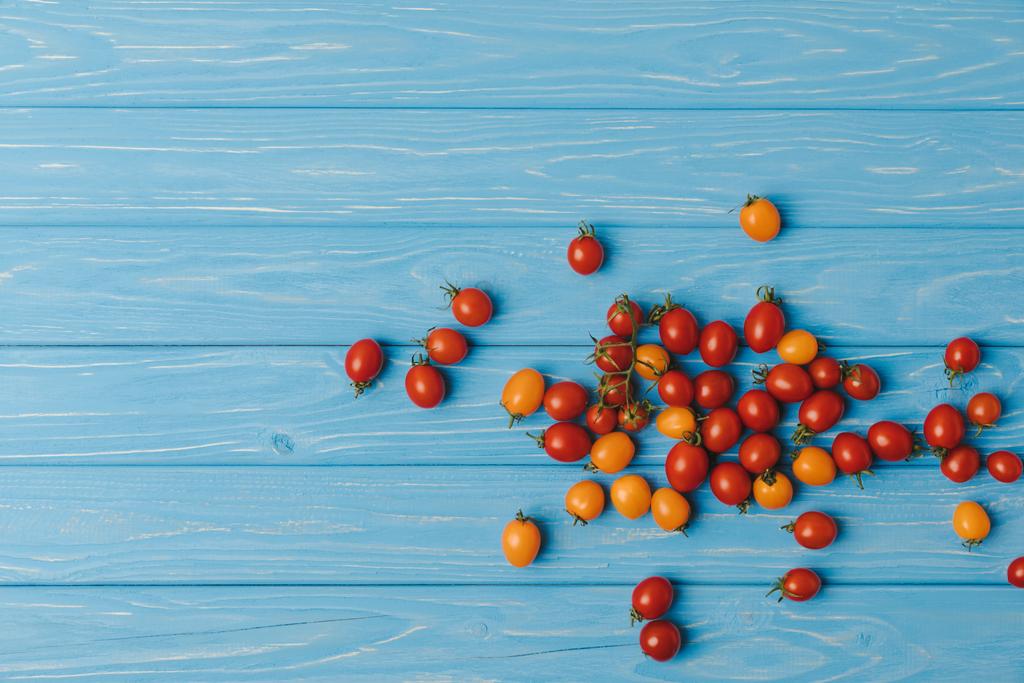 Draufsicht auf rote und orangefarbene Kirschtomaten auf blauen Tisch - Foto, Bild
