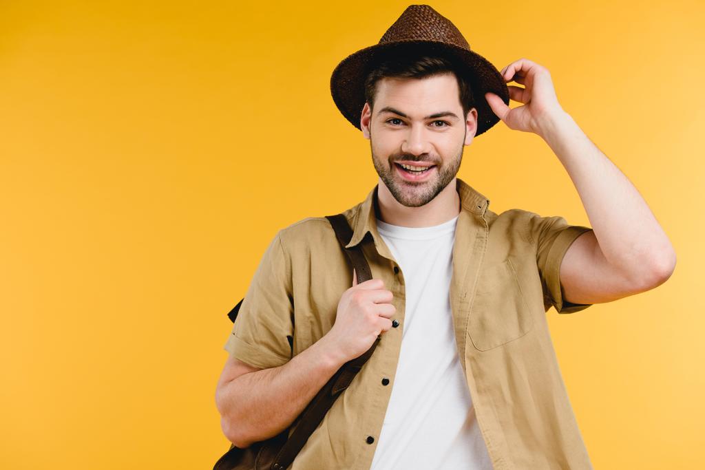 knappe jonge man hoed aanpassen en lachend op camera geïsoleerd op geel  - Foto, afbeelding
