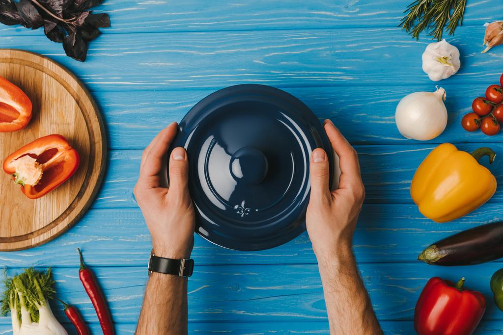 image recadrée de l'homme mettant casserole sur table bleue
 - Photo, image