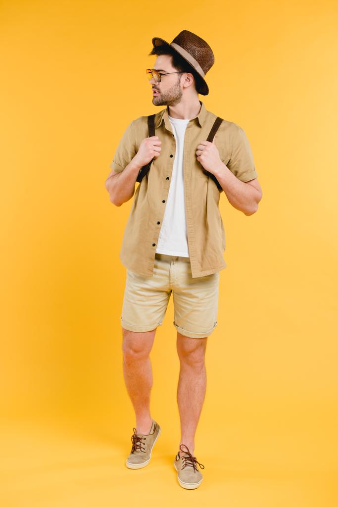 pohledný mladý muž s batoh při pohledu od izolovaných na žluté - Fotografie, Obrázek