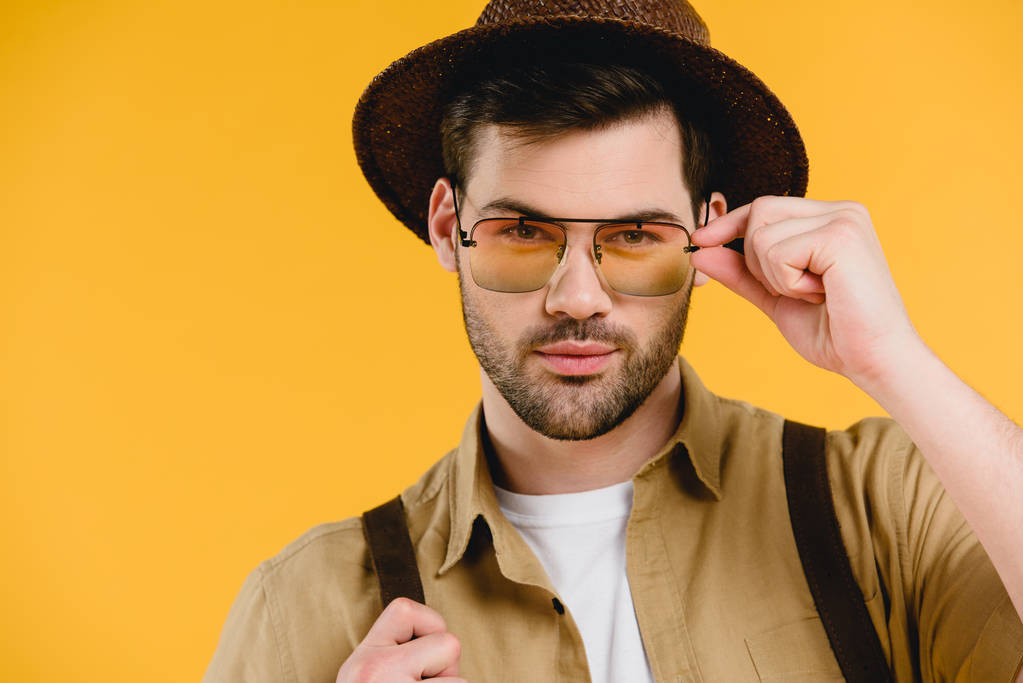 портрет красивого молодого чоловіка в капелюсі і сонцезахисних окулярах дивиться на камеру ізольовано на жовтому
 - Фото, зображення