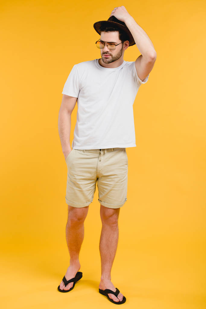 guapo barbudo joven en pantalones cortos y chanclas mirando hacia otro lado aislado en amarillo
 - Foto, imagen