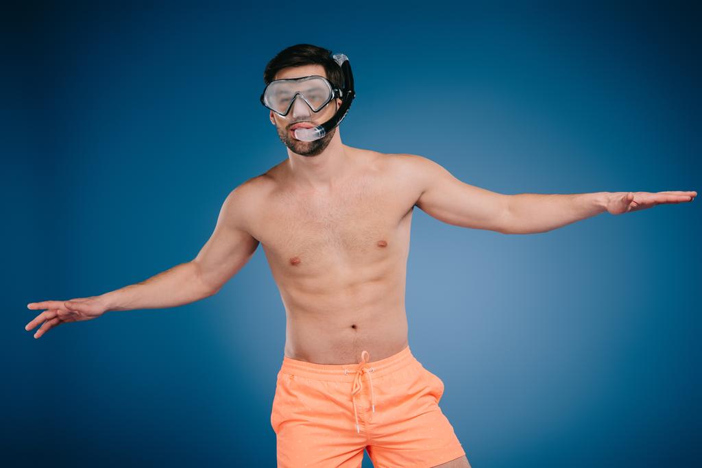 schöner junger Mann in kurzen Hosen mit Schnorchel und Tauchermaske auf blauem Grund - Foto, Bild