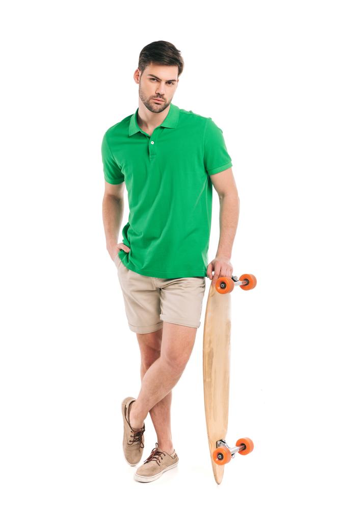 стильный молодой человек, опирающийся на скейтборд и смотрящий на камеру, изолированную на белом
 - Фото, изображение