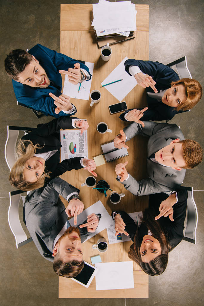 Pohled shora se spolupracovníky ukazující prostředníčkem a sedí u stolu v kanceláři - Fotografie, Obrázek