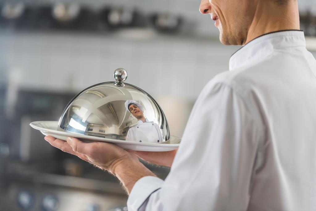 περικομμένη εικόνα όμορφος σεφ πλατώ με καπάκι σε κουζίνα εστιατορίου - Φωτογραφία, εικόνα