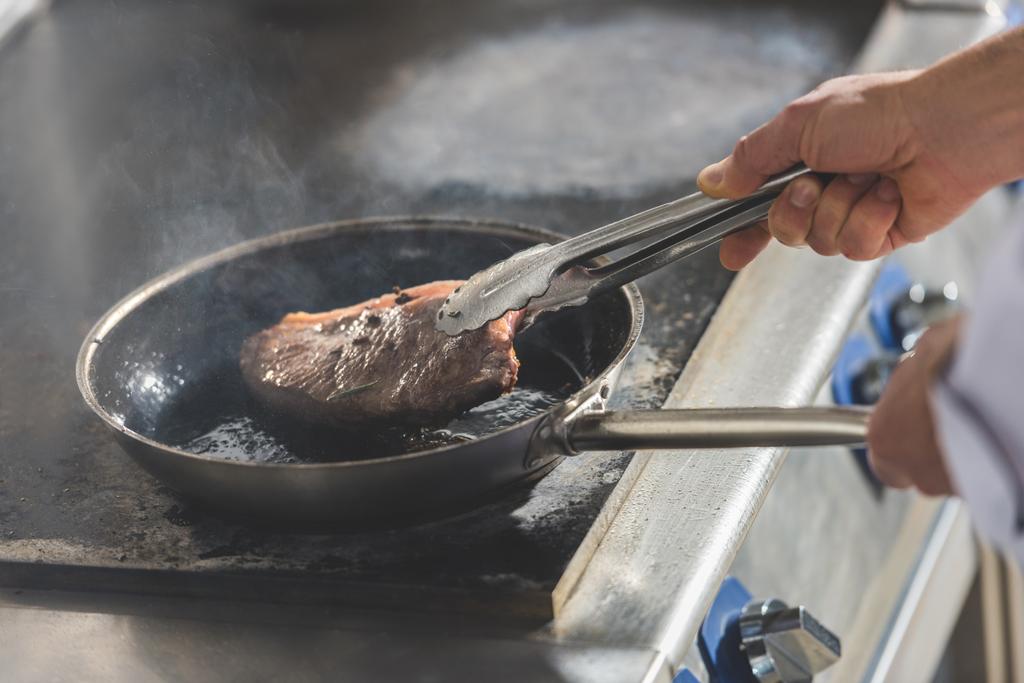 обрезанный образ жарки стейка шеф-повара на кухне ресторана
 - Фото, изображение