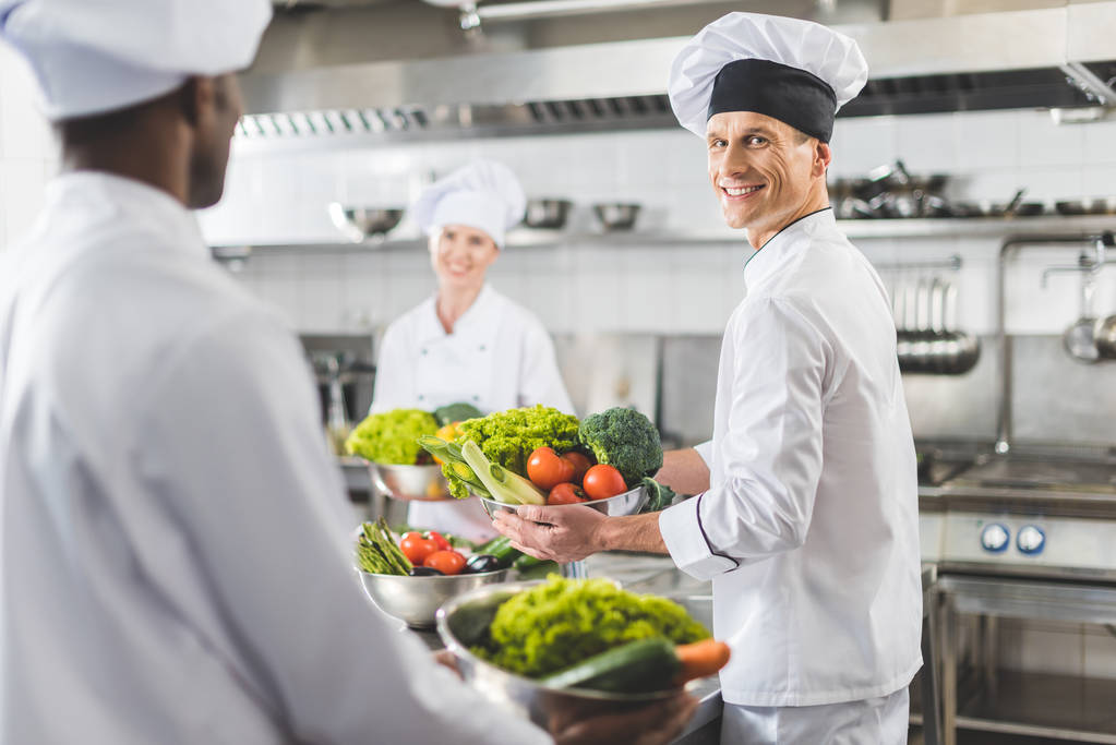 мультикультурні кухарі тримають миски з овочами на кухні ресторану
 - Фото, зображення