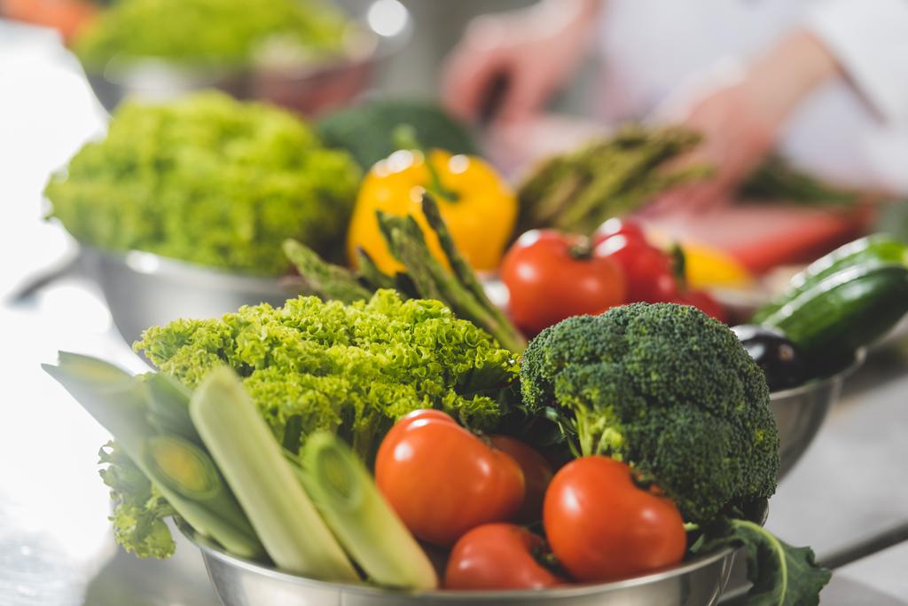 обрезанный образ приготовления шеф-повара на кухне ресторана с спелыми овощами на переднем плане
 - Фото, изображение