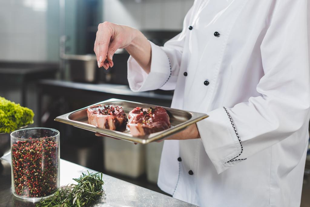 Oříznout obrázek šéfkuchař přidávání koření na syrové steaky v restauraci kitchen - Fotografie, Obrázek