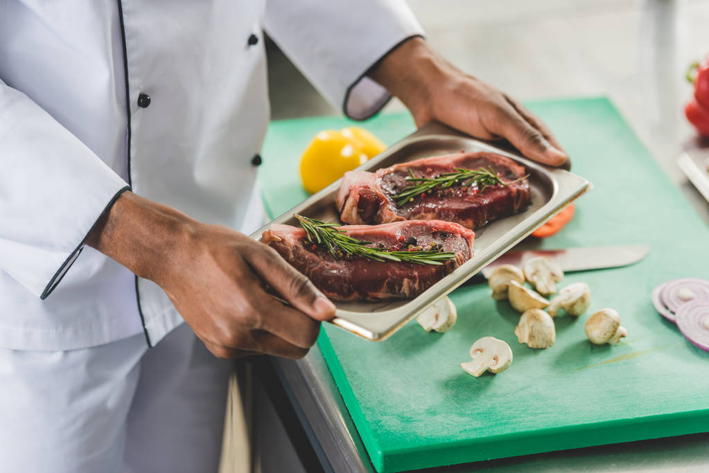 rajattu kuva afrikkalainen amerikkalainen kokki tilalla tarjotin raaka liha ravintola keittiö
 - Valokuva, kuva