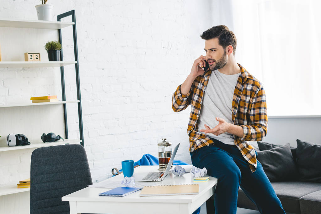 Молодий чоловік сидить на столі і розмовляє по телефону в легкому офісі
 - Фото, зображення