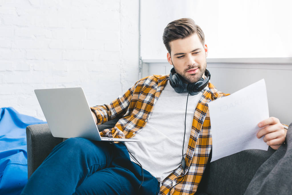 Podnikatel holing laptop a papíru sedí na gauči doma kancelář - Fotografie, Obrázek