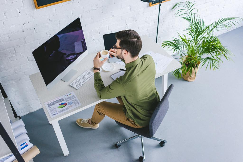 Молодий чоловік дивиться на екран комп'ютера і п'є каву вдома
 - Фото, зображення