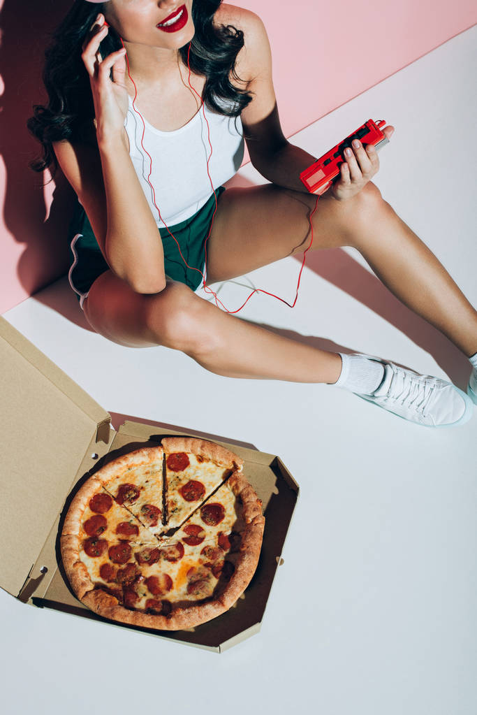 Schnappschuss einer lächelnden Frau mit Retro-Musikplayer und Lieferbox mit Pizza auf rosa Hintergrund - Foto, Bild