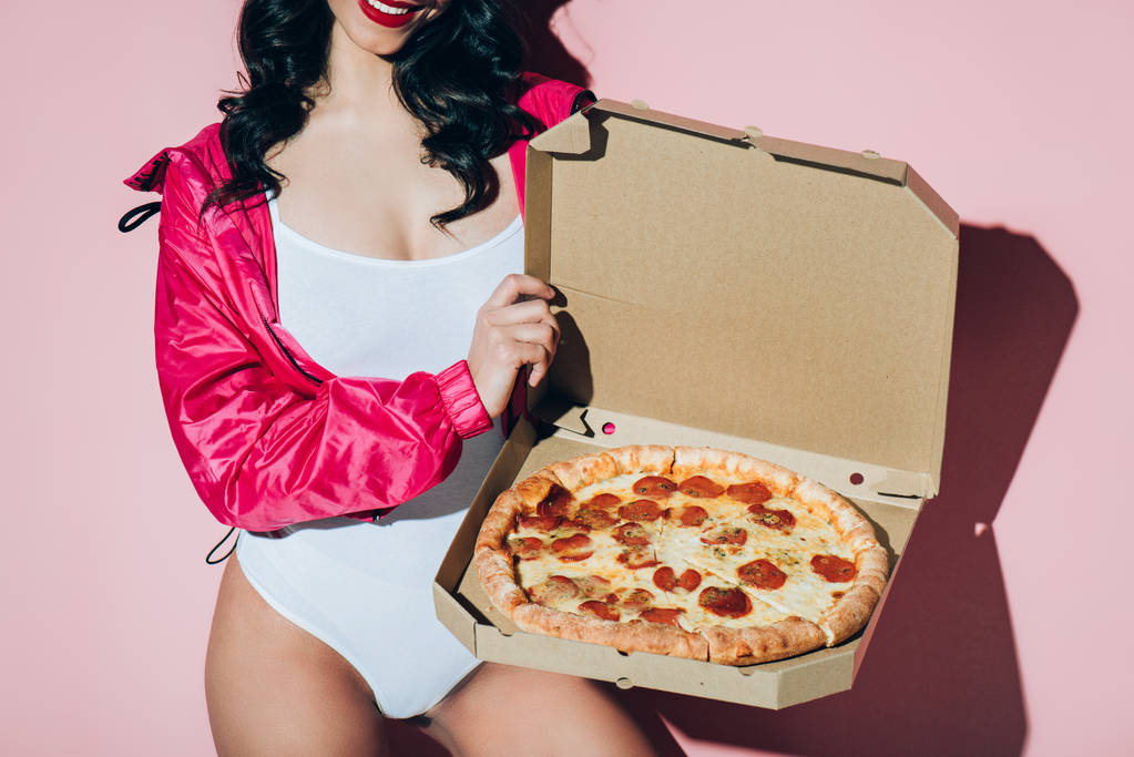 περικοπεί shot γυναίκα στο λευκό κορμάκι που κρατάει παράδοσης κουτί με πίτσα σε ροζ φόντο - Φωτογραφία, εικόνα