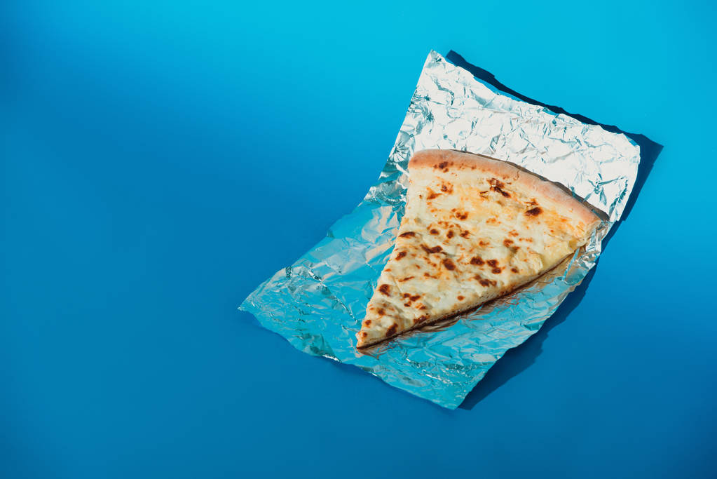Vista de cerca del pedazo de pizza italiana sobre papel de aluminio sobre fondo azul
 - Foto, imagen
