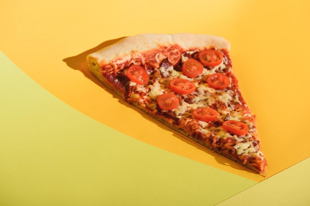κλείνω πάνω θέα του κομματιού του Ιταλική Πίτσα με ντοματίνια στο πολύχρωμο σκηνικό - Φωτογραφία, εικόνα
