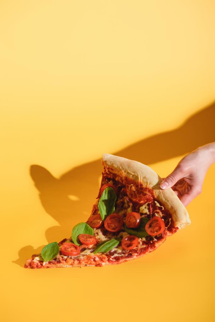 vue partielle de la femme tenant un morceau de pizza avec des tomates cerises à la main sur fond jaune
 - Photo, image