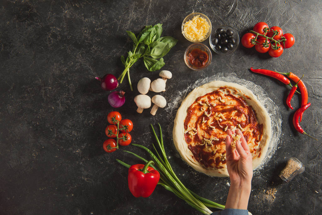 暗い卓上にイタリアのピザを料理しながら生地に粉チーズを入れて女性のショットをトリミング - 写真・画像
