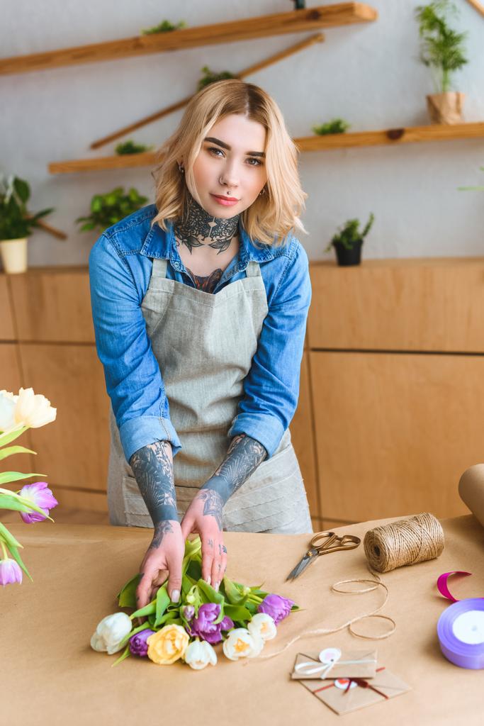 bela jovem florista feminina em avental olhando para a câmera enquanto trabalhava na loja de flores
 - Foto, Imagem