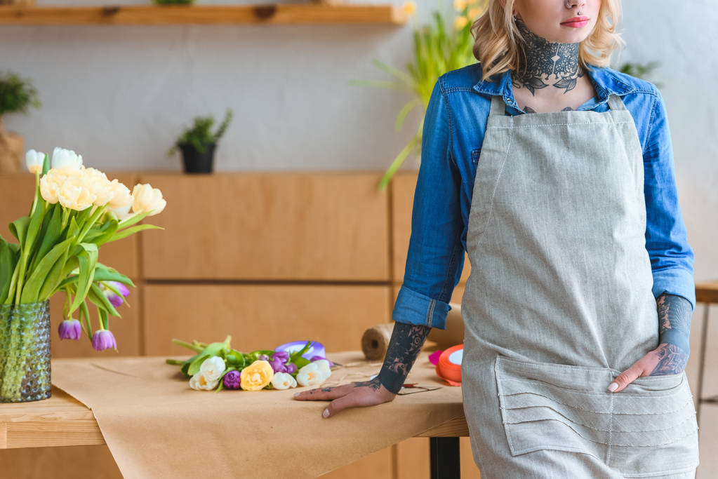 обрезанный снимок флориста в фартуке, прислоненный к столу красивыми цветами тюльпана
 - Фото, изображение