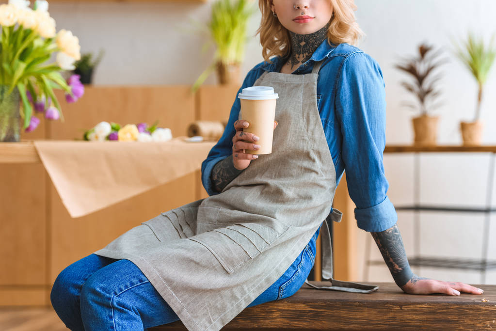 обрезанный снимок флориста в фартуке держит кофе, чтобы пойти
 - Фото, изображение