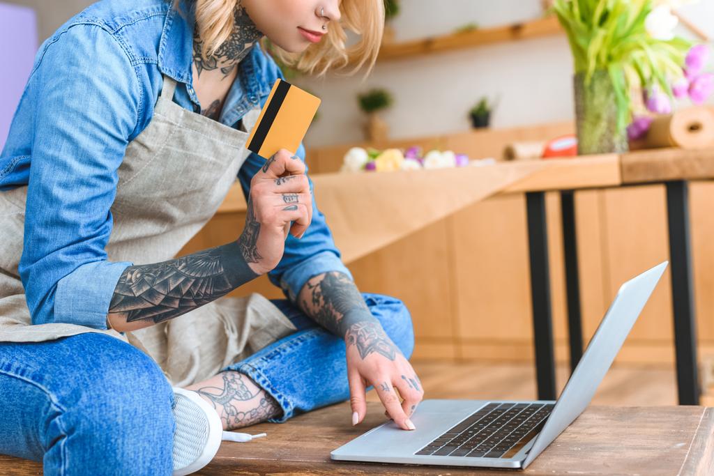 tiro recortado de florista jovem segurando cartão de crédito e usando laptop
 - Foto, Imagem