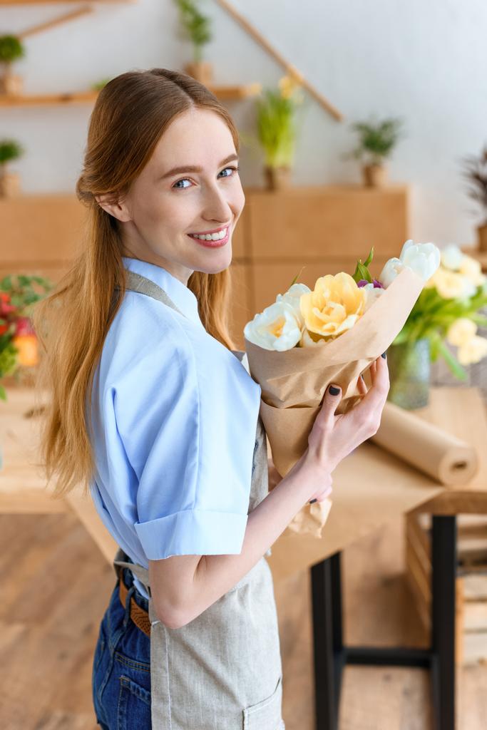 nuori nainen kukkakauppias tilalla kaunis kimppu tulppaanit ja hymyilee kameran edessä kukkakauppa
  - Valokuva, kuva