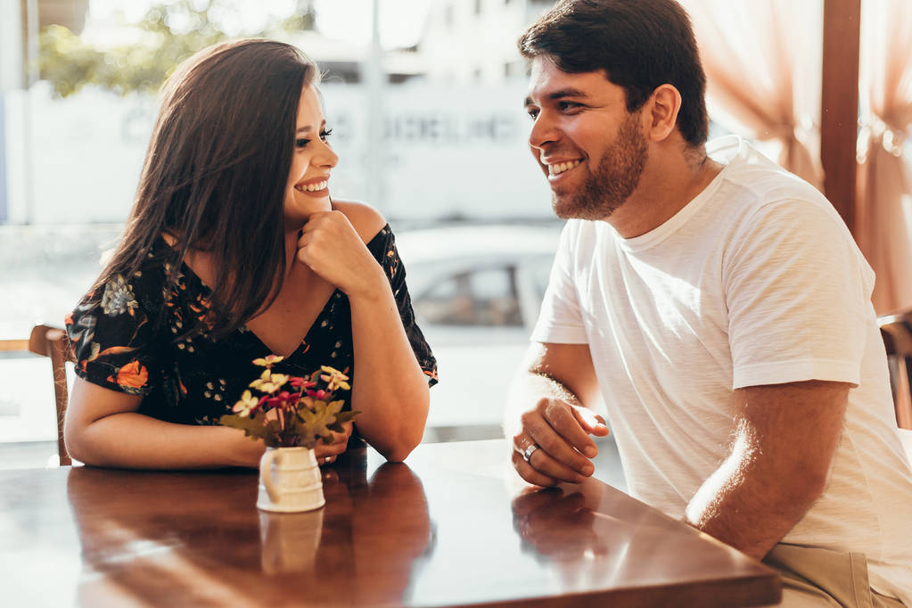 Молодая пара влюбленных сидит в кафе, разговаривает и наслаждается временем, проведенным друг с другом
. - Фото, изображение