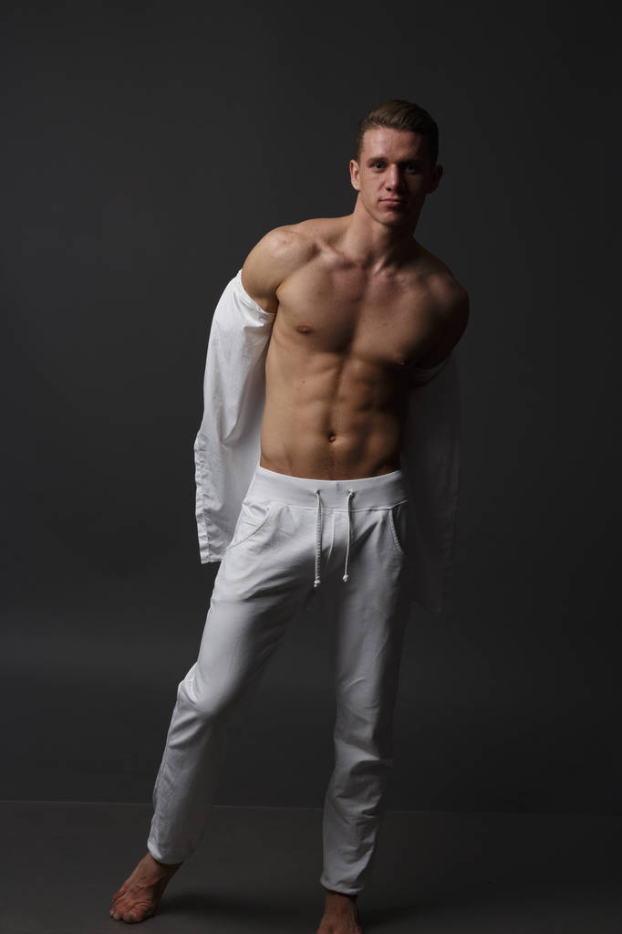 un tipo con un torso desnudo, en pantalones blancos, y en una camisa blanca, se para sobre un fondo gris
 - Foto, imagen