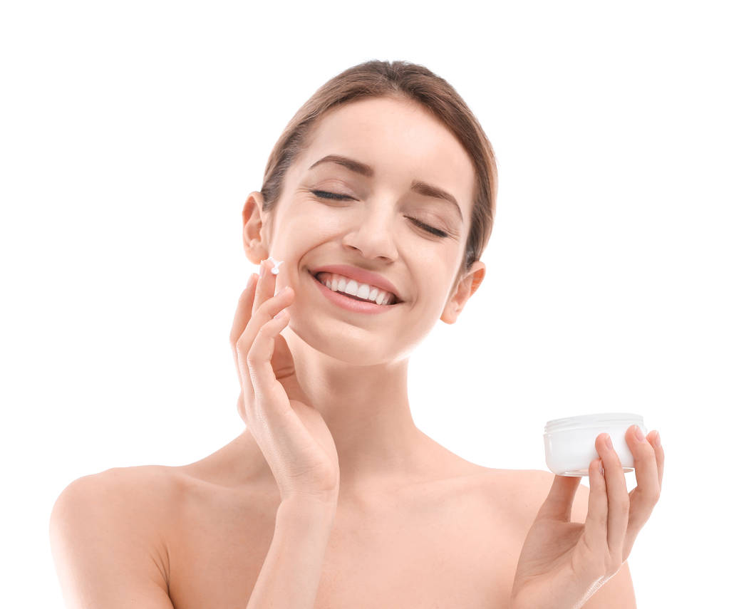 Mujer joven aplicando crema facial sobre fondo blanco - Foto, imagen