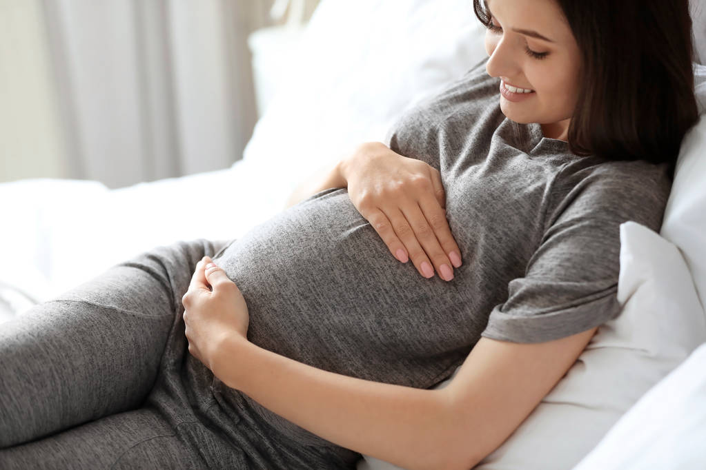 Fiatal terhes nő ágyon otthon - Fotó, kép