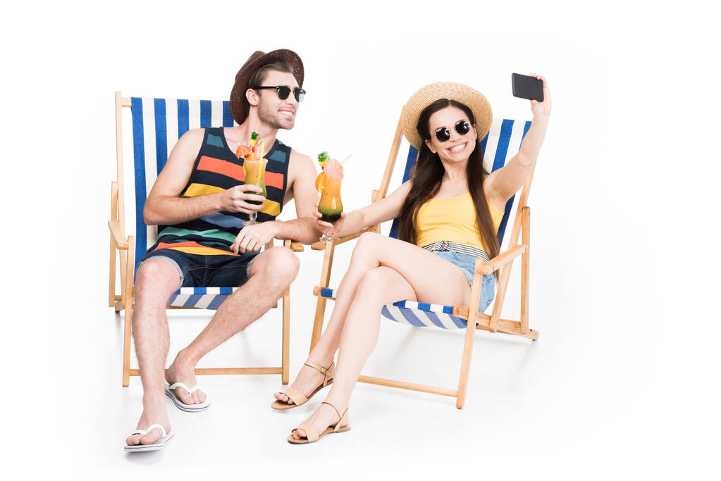 couple relaxing on beach chairs with cocktails and taking selfie, isolated on white - Photo, Image