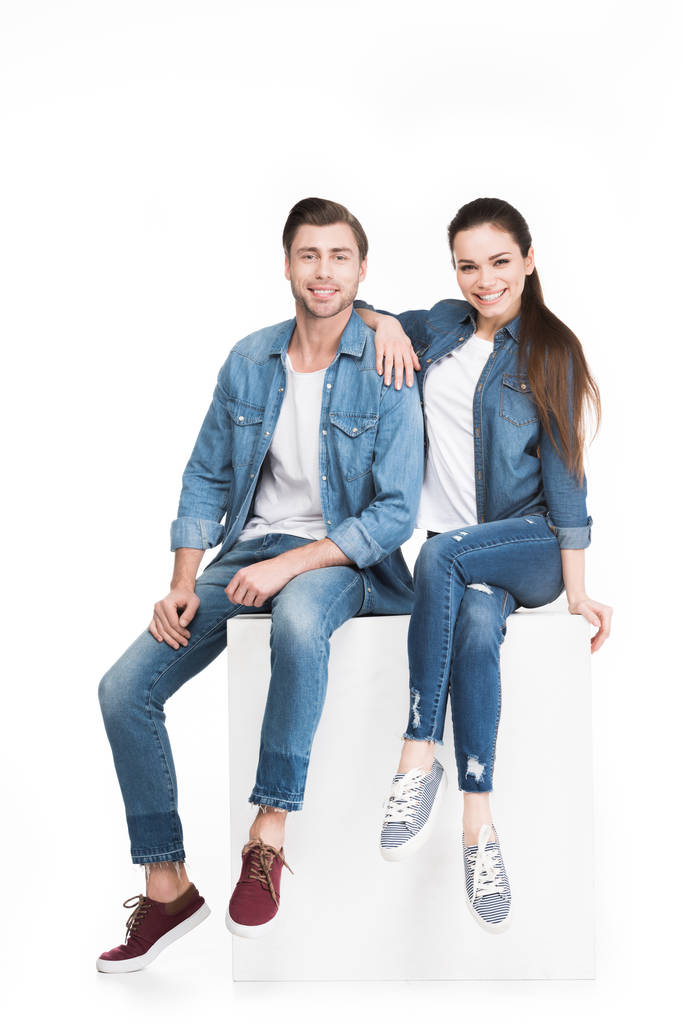 couple souriant en jeans assis sur cube blanc et regardant la caméra, isolé sur blanc
 - Photo, image