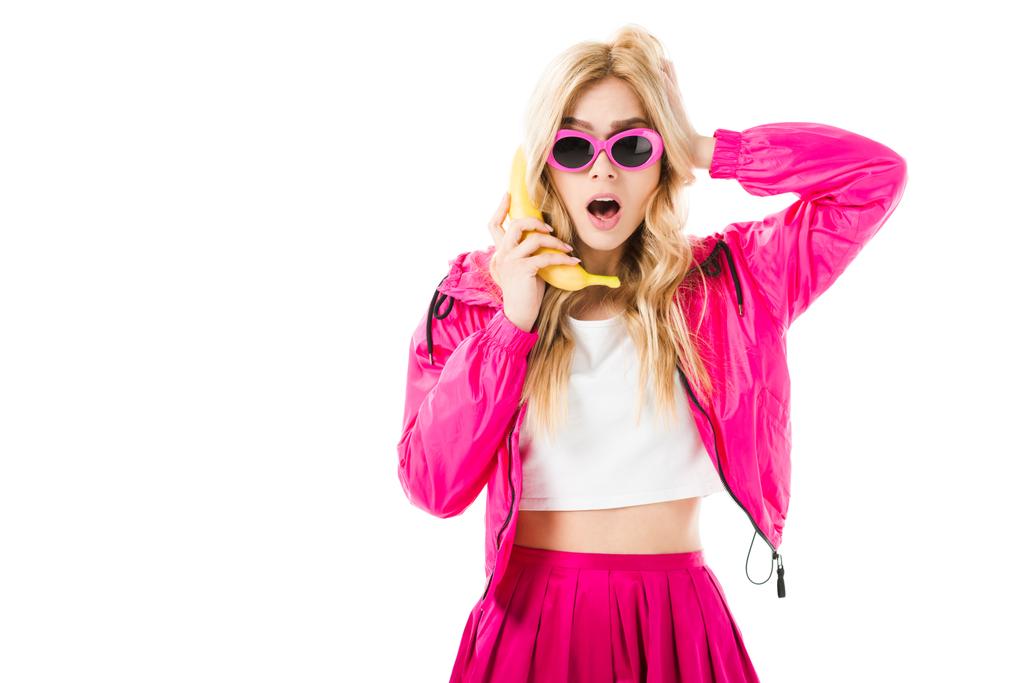 Fiatal meglepett lány visel rózsaszín segítségével a banán, mint elszigetelt fehér telefon - Fotó, kép