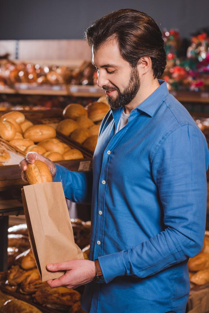 Zijaanzicht van glimlachende man kiezen brood in hypermarkt - Foto, afbeelding