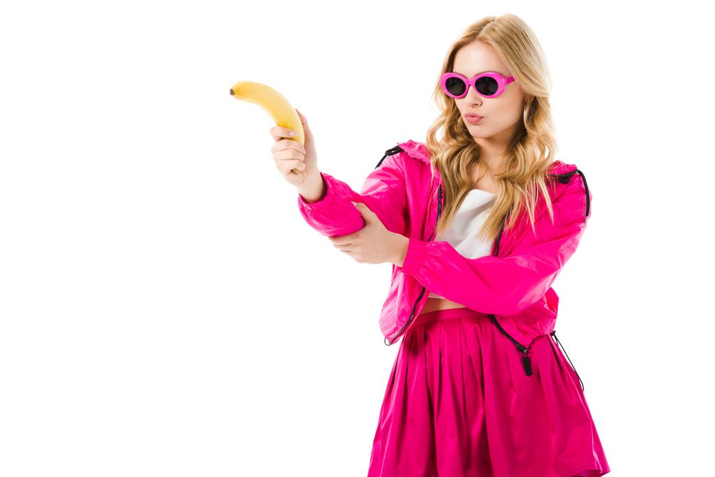 Attractive young woman dressed in pink holding banana like gun isolated on white - Photo, Image