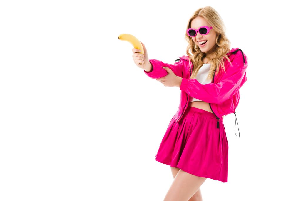 Attractive young woman dressed in pink shooting from banana isolated on white - Photo, Image