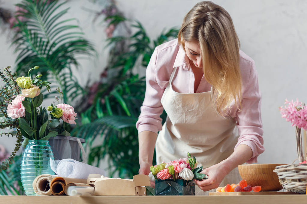 Photo of blonde florist making bouquet of marshmallows, flowers - Photo, Image
