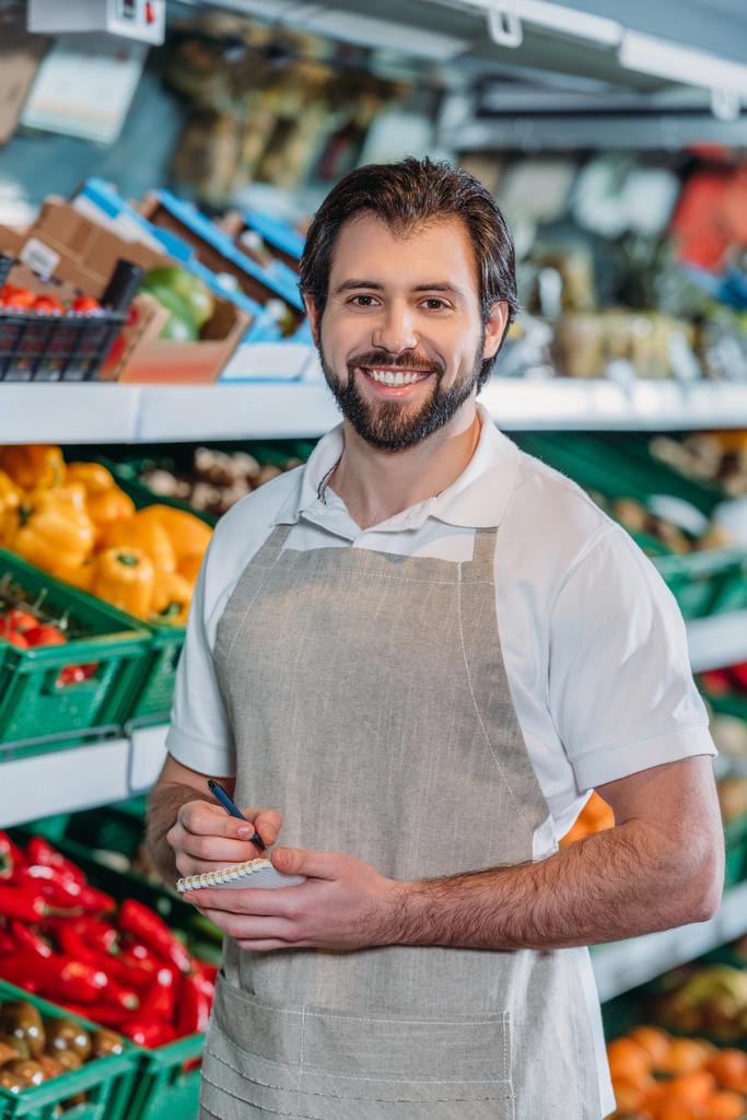 portrét s úsměvem prodavače v zástěře s notebookem v supermarketu - Fotografie, Obrázek